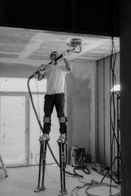 Man on stilts painting the ceiling of a building under construction