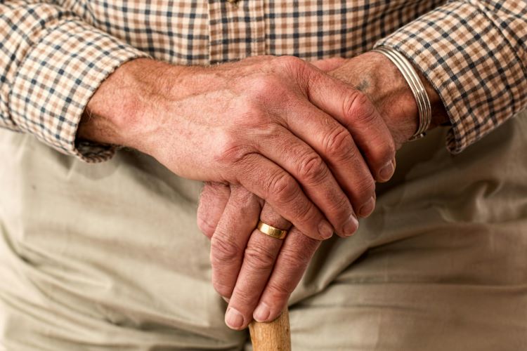 Elderly mans hands crossed holding a walking stick